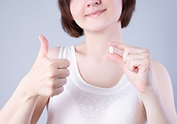 Nose-to-chest view of a woman giving thumbs up and holding extracted tooth