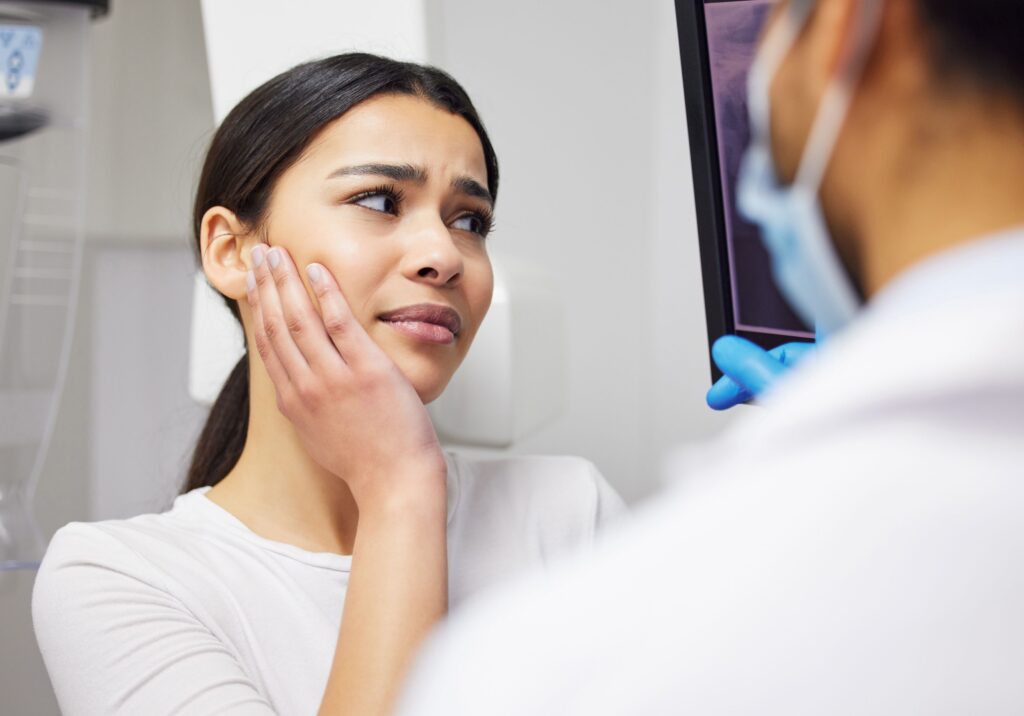 Woman with brown hair looking at X-ray with dentist holding hand to jaw